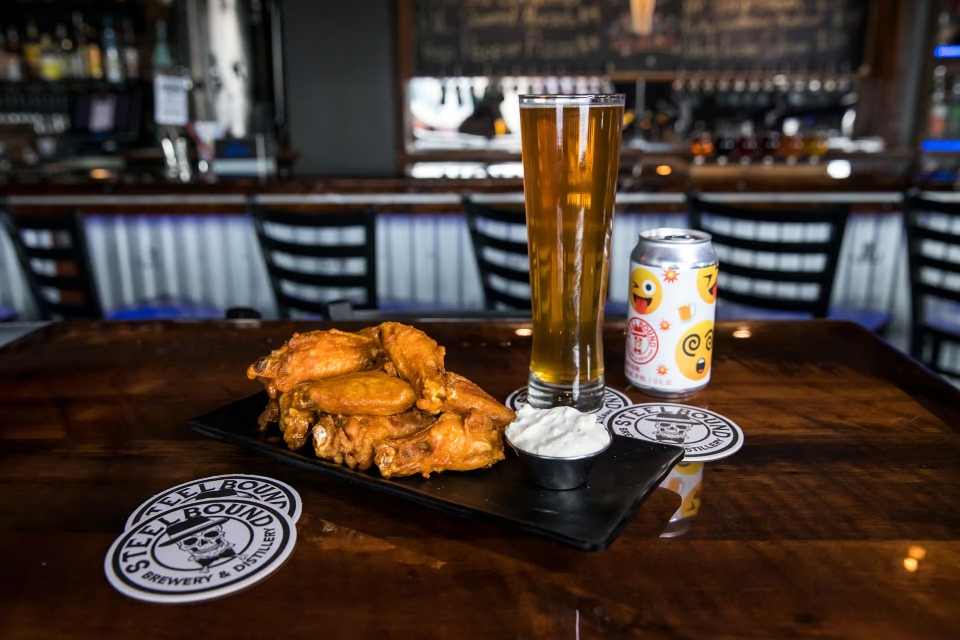 A plate of chicken wings, a glass of beer and a can of beer at Steelbound Brewery & Distillery